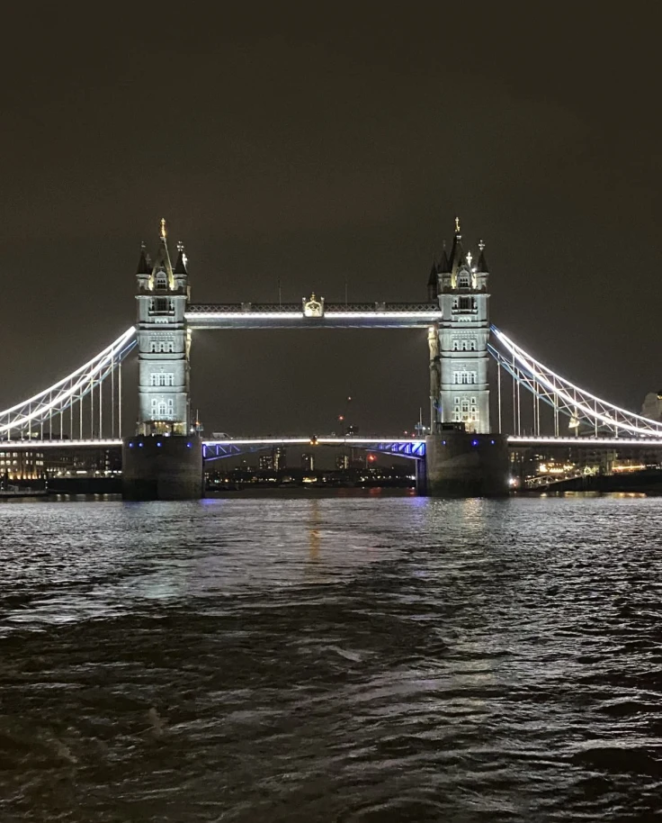 A view of the bridge in London lit up at night with the river in front.