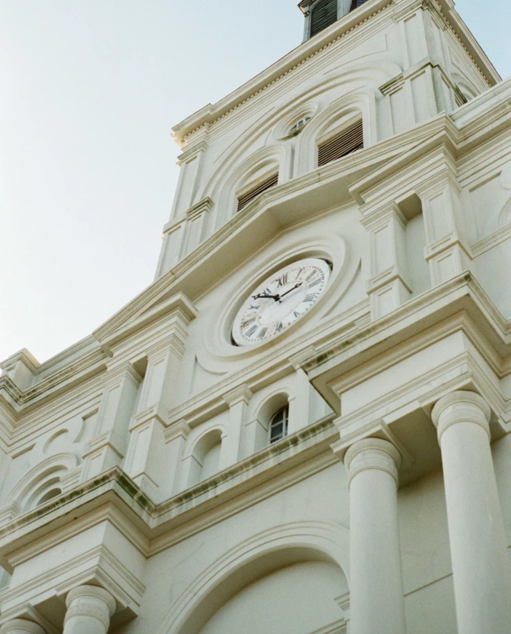 A low-angled shot of a white-colored building with a clock in the middle located close to the Mercantile Hotel, New Orleans