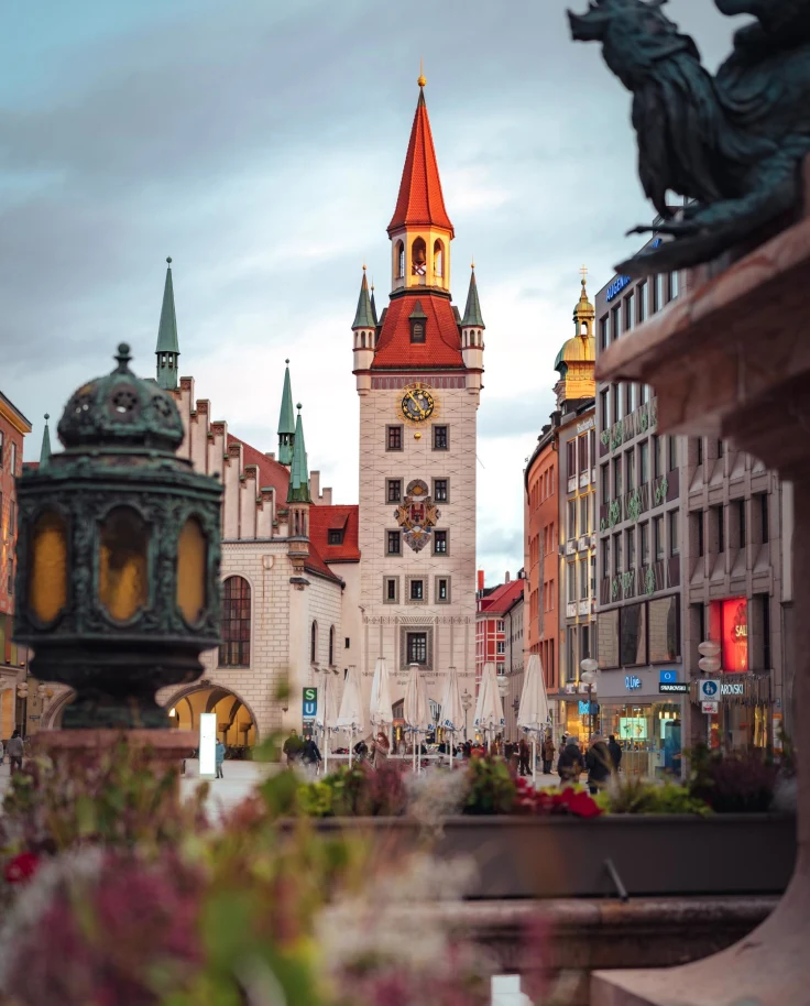 View of iconic tower in Munich from fountain on bright but cloudy day.