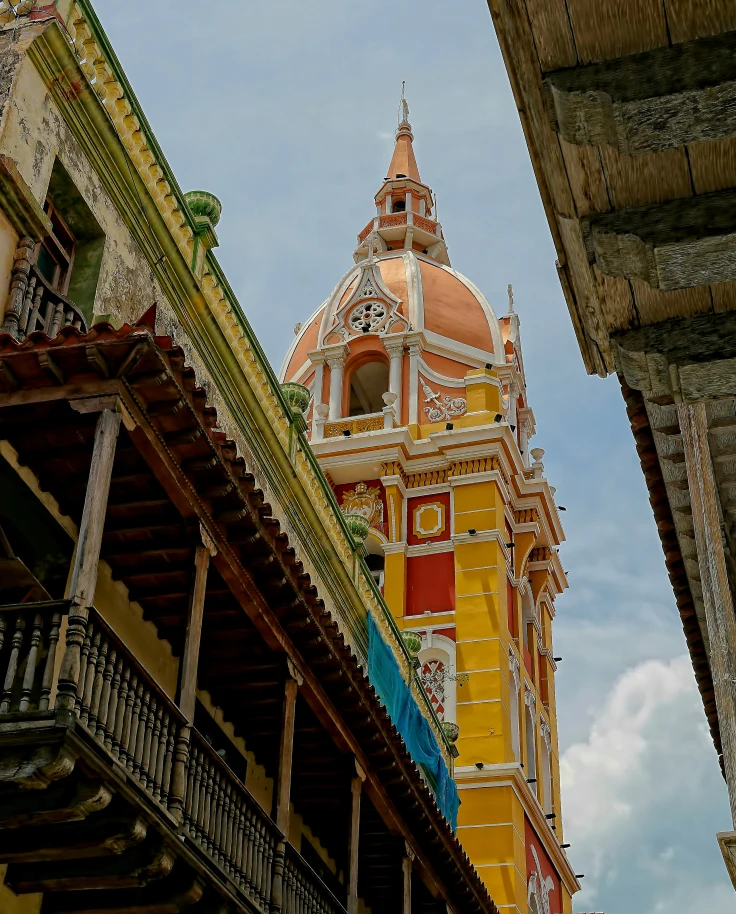 A yellow cathedral as seen from between colorful city streets.