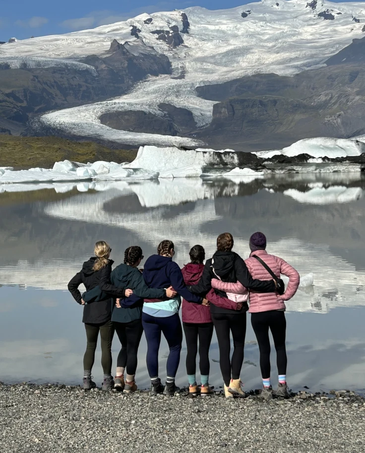 6 girls facing a lake with snow covered mountains.