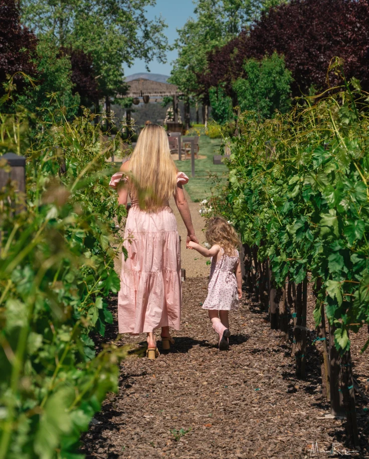 Chelsea and a little girl in pink dresses walking on a path through flowers away from the camera.