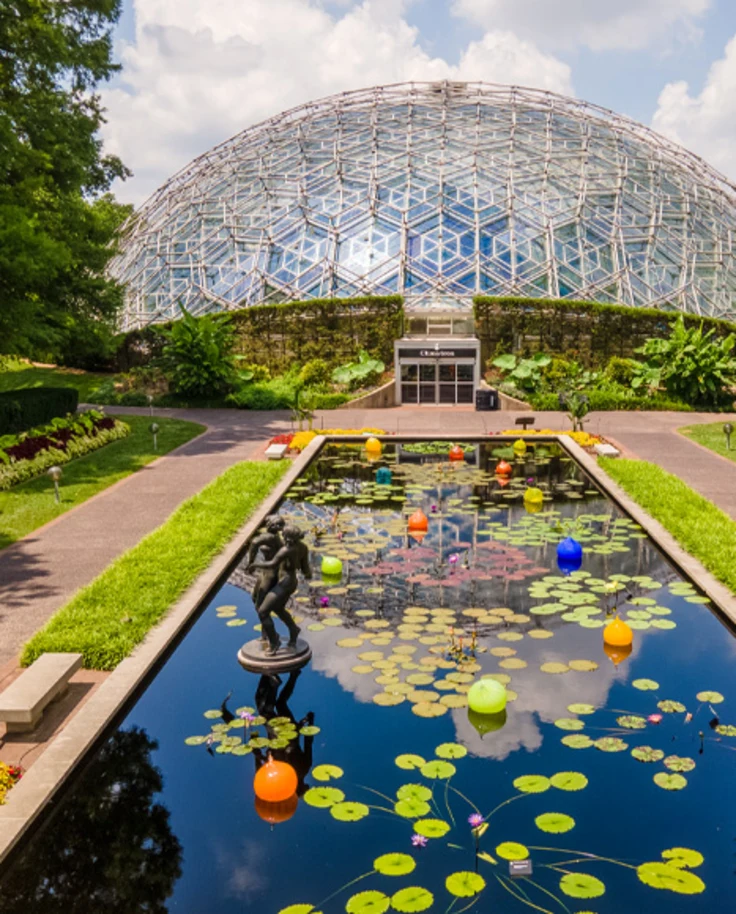 A view of a lily pad pond with beautifully manicured lawns, pathways and an elaborate glass dome in the center of the image.