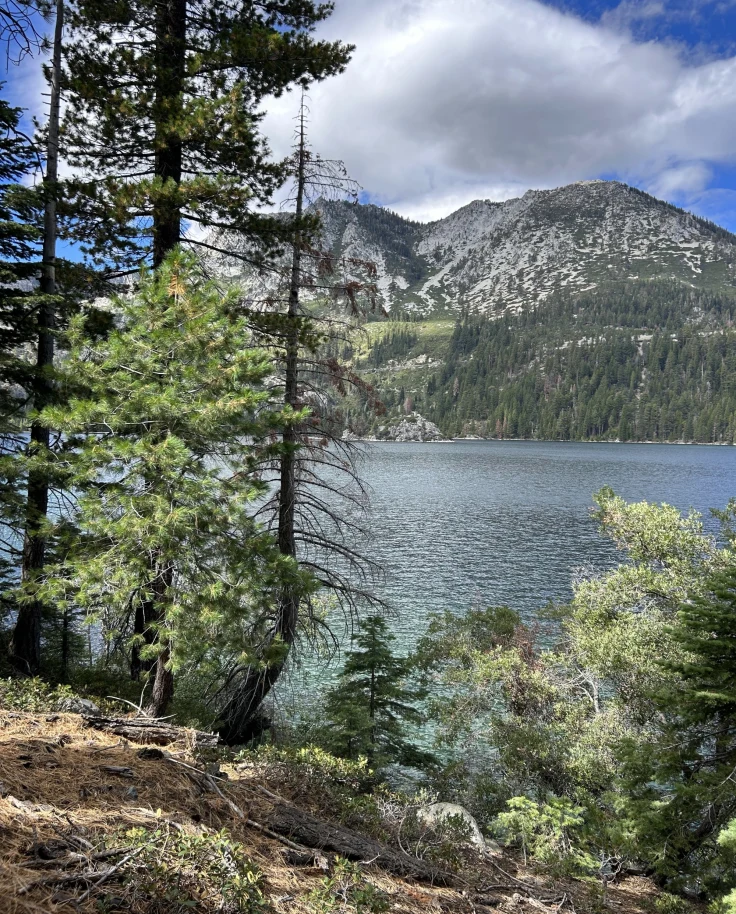 A scenic lake with surrounding mountains and trees is shown under a partly cloudy sky.
