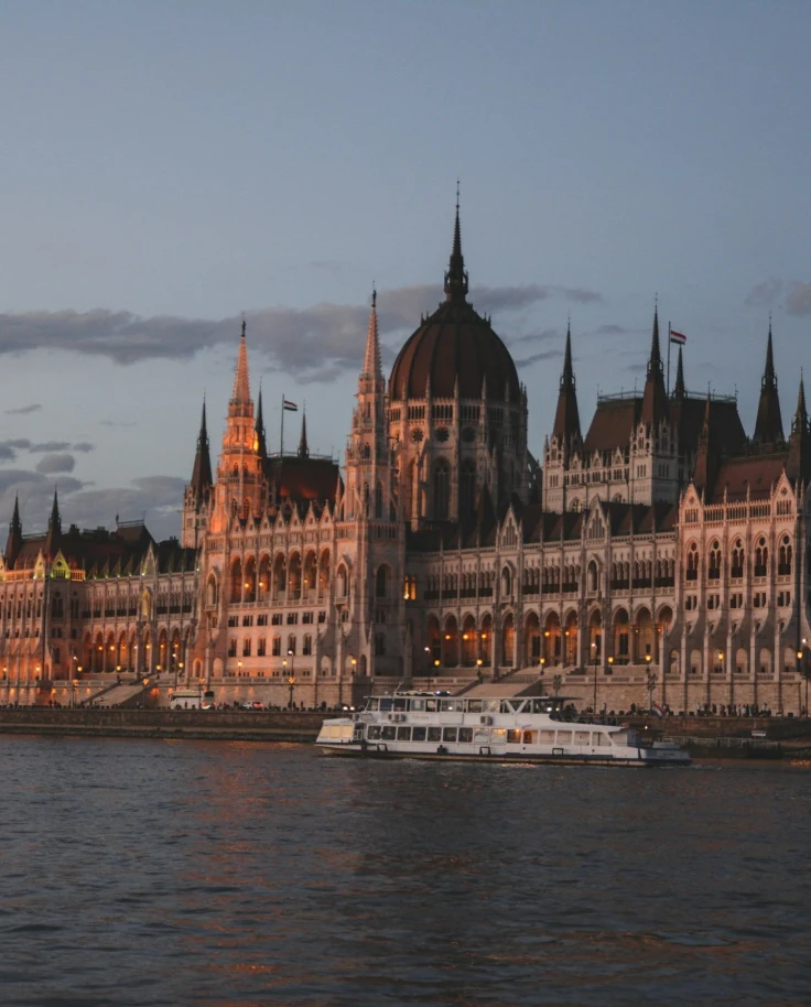 Sunset cruise at Danube River – a white boat on the river in front of The Parliament House of Hungary.