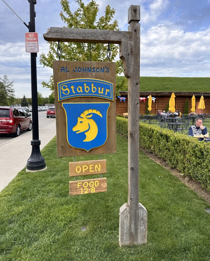 The image portrays a vibrant outdoor sign for “Al Johnson’s Swedish Restaurant & Butik,” featuring a blue and yellow logo with a stylized goat, indicating the cultural theme and unique appeal of the establishment.