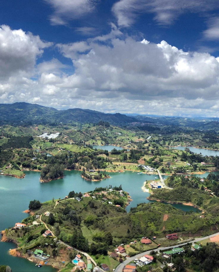 A panoramic view of a lush, green landscape with a winding road and multiple bodies of water surrounded by trees.