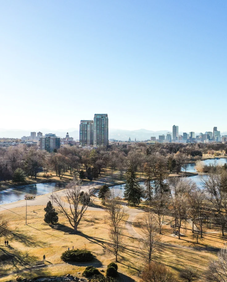 aerial view of a park with trees where people like to spend weekends in Denver, and the city skyline with mountains in the background