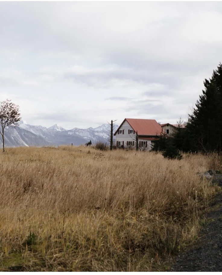 a solitary cabin on a grassy meadow in front of snowy peaks