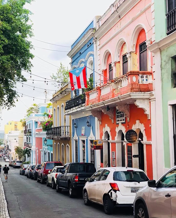 colorful houses with balconies line a street parked with cars