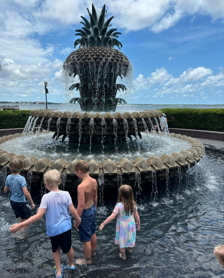 Kids playing around pineapple shaped fountain.