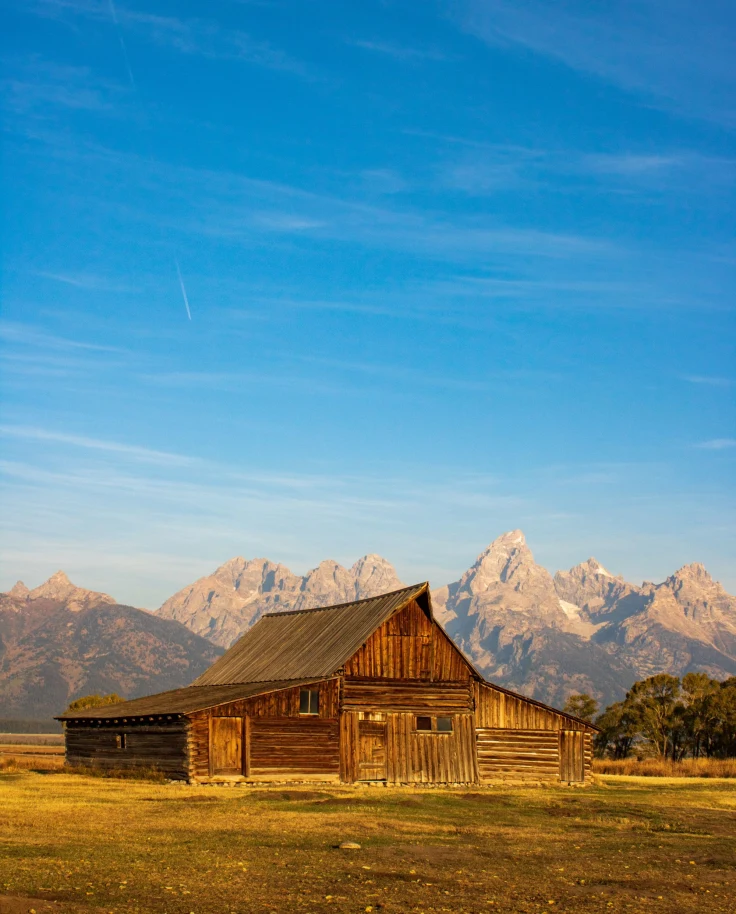 historic barn on the flats beneath a vast mountain range with a clear blue sky above