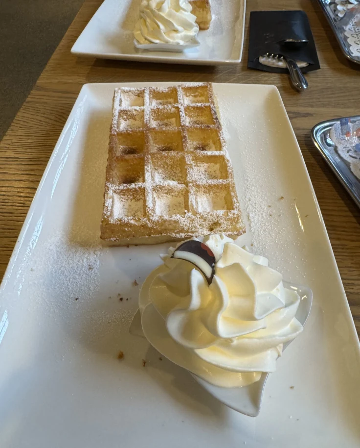 Plates of Belgian Waffles and cream, topped with powdered sugar.