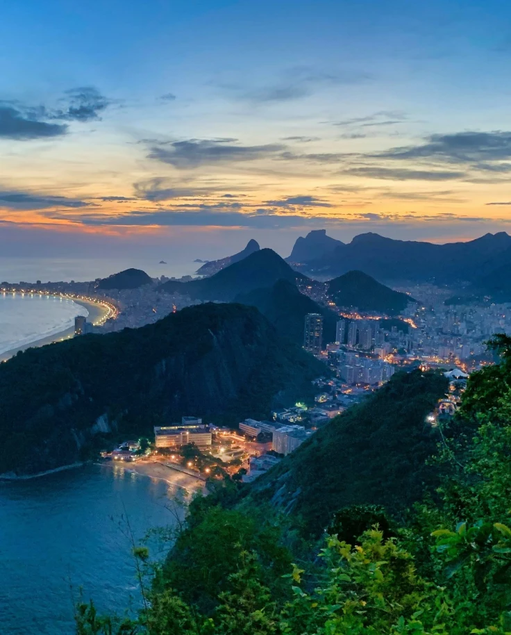 Aerial view of city nestled between mountains and ocean at night with tall illuminated buildings