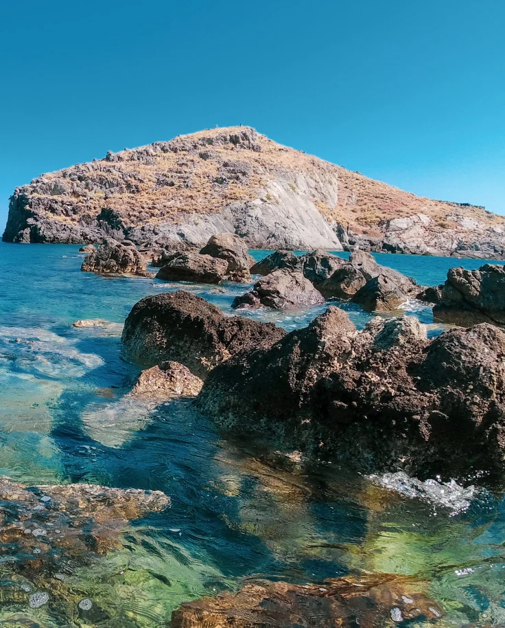 blue clear water with tan rocks and blue sky in Crete