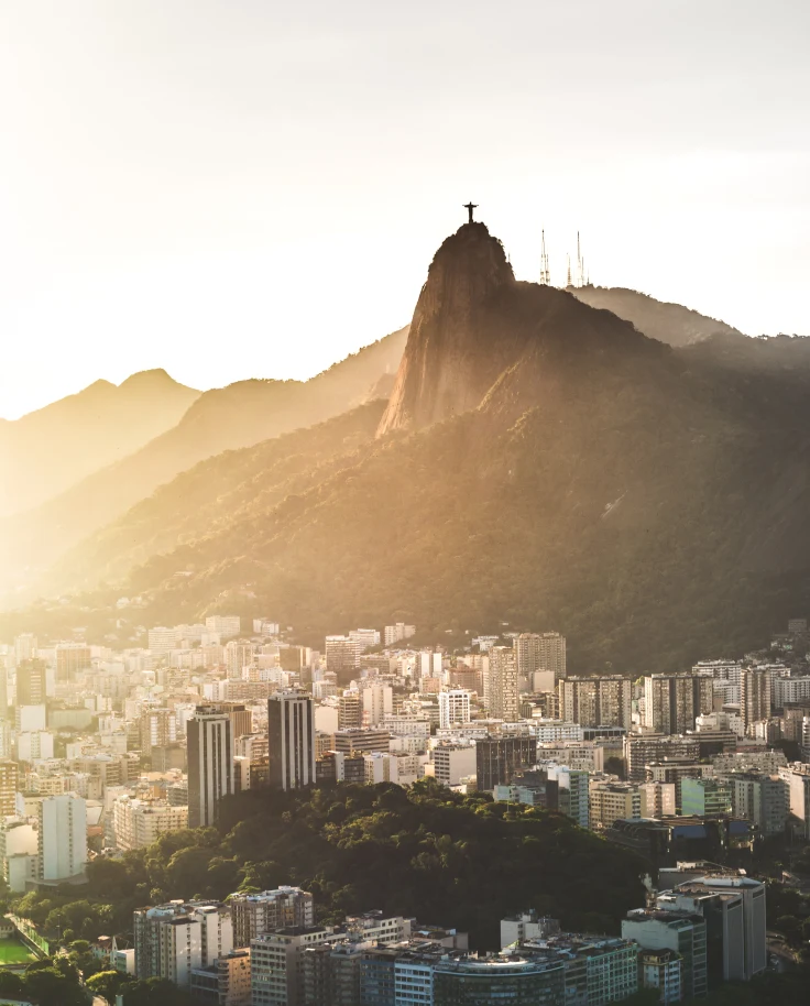 Sunset from Sugarloaf mountain in Rio de Janeiro in Brazil overlooking the city full of white buildings and the large drastic mountains.