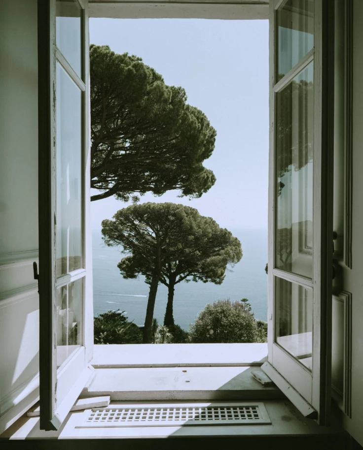 open white window overlooking green trees and the sea below