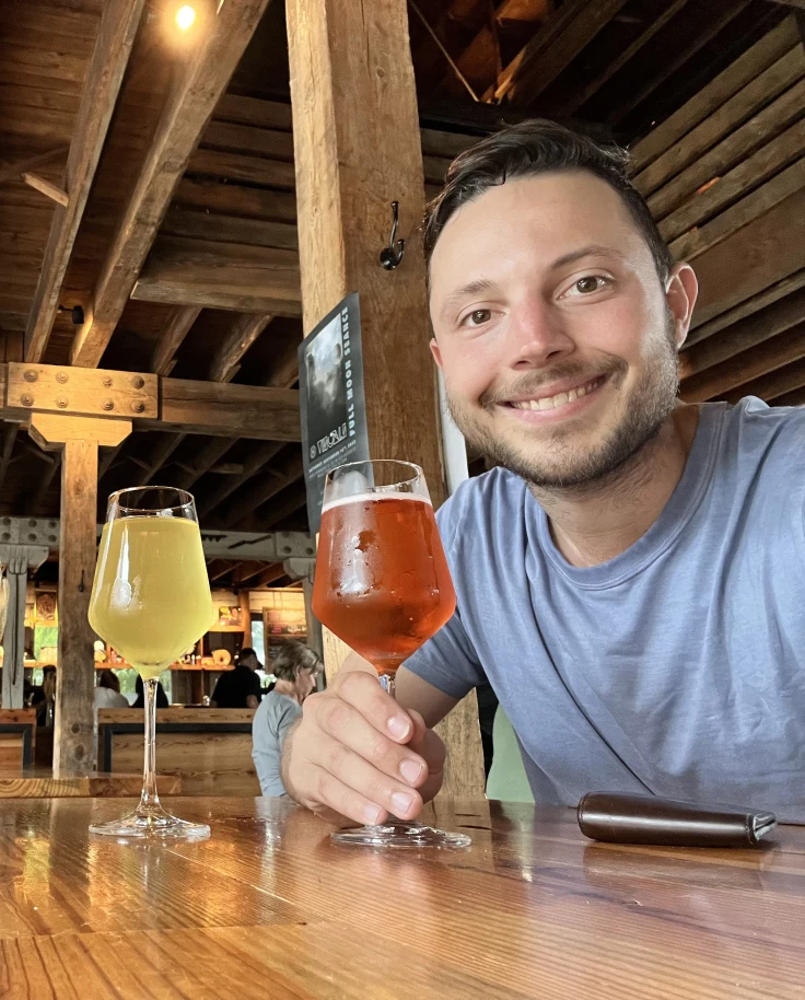 Steven Lawrence taking a selfie with two beers at a wooden bar at AVL Forestry Camp
