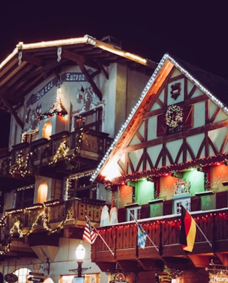 The exterior of a wooden chalet decorated with Christmas lights, an American and German flag.