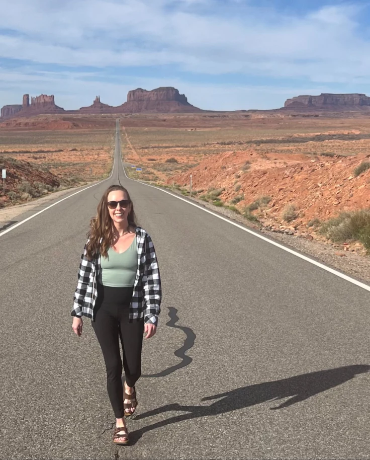 The advisor walks down the median line of a two-lane highway with desert formations in the background.