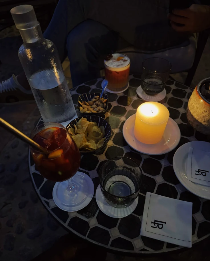 A table set with various drinks and snacks, illuminated by candlelight for an intimate atmosphere.