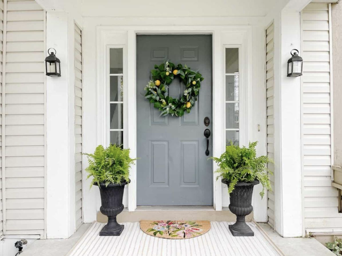 A grey door with a wreath and potted plantsDescription automatically generated