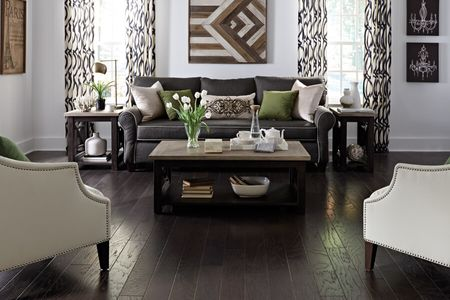 A modern living room with dark hardwood floors, a dark grey sofa, and light-colored walls.