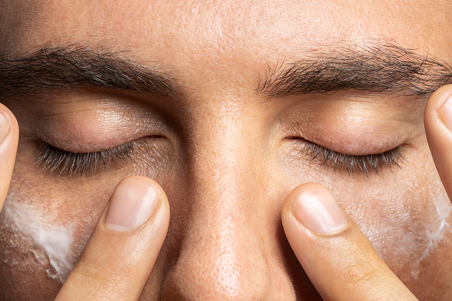 A closeup of a man applying skin care product to his face