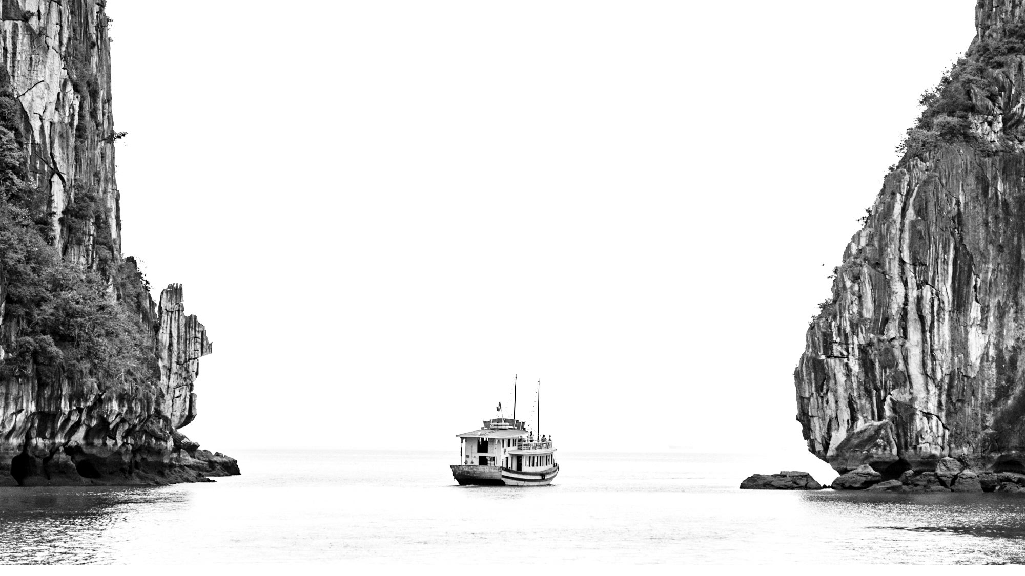 Black and white picture of a boat sailing between two islands