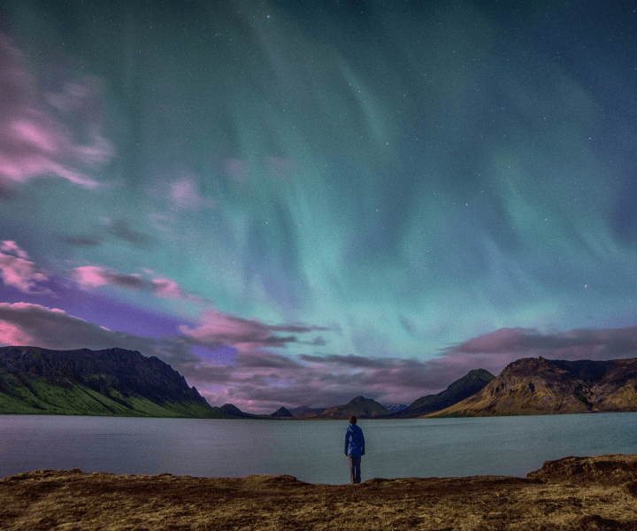 Person standing at lake looking at northern lights in sky