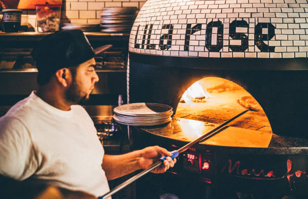 Team member cooking pizza in the custom oven, names 'Lila Rose'