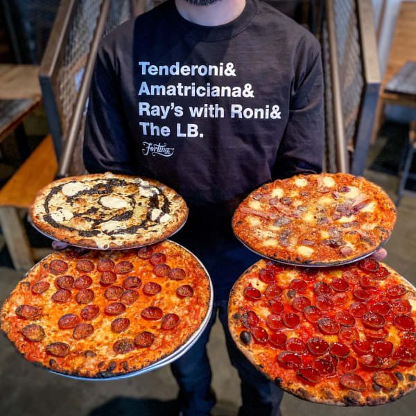 An employee holding 4 pizzas, modeling some of the clothing merch available at the Fortina Shop