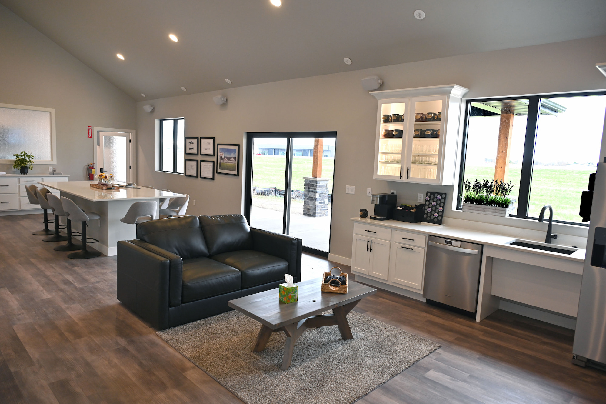 Open-concept commercial construction interior featuring a modern kitchen, meeting area with bar seating and leather couch