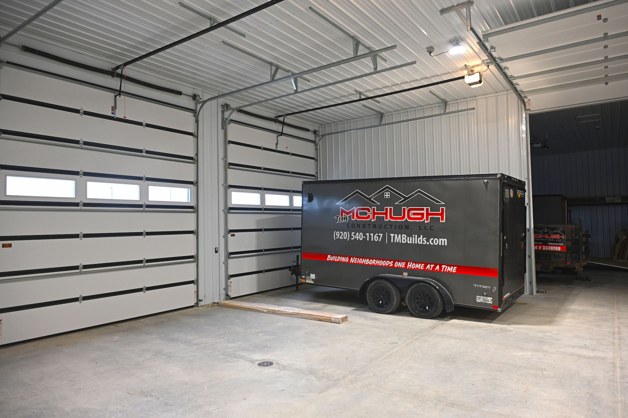 Interior garage with construction trailer parked in front of oversized overhead doors