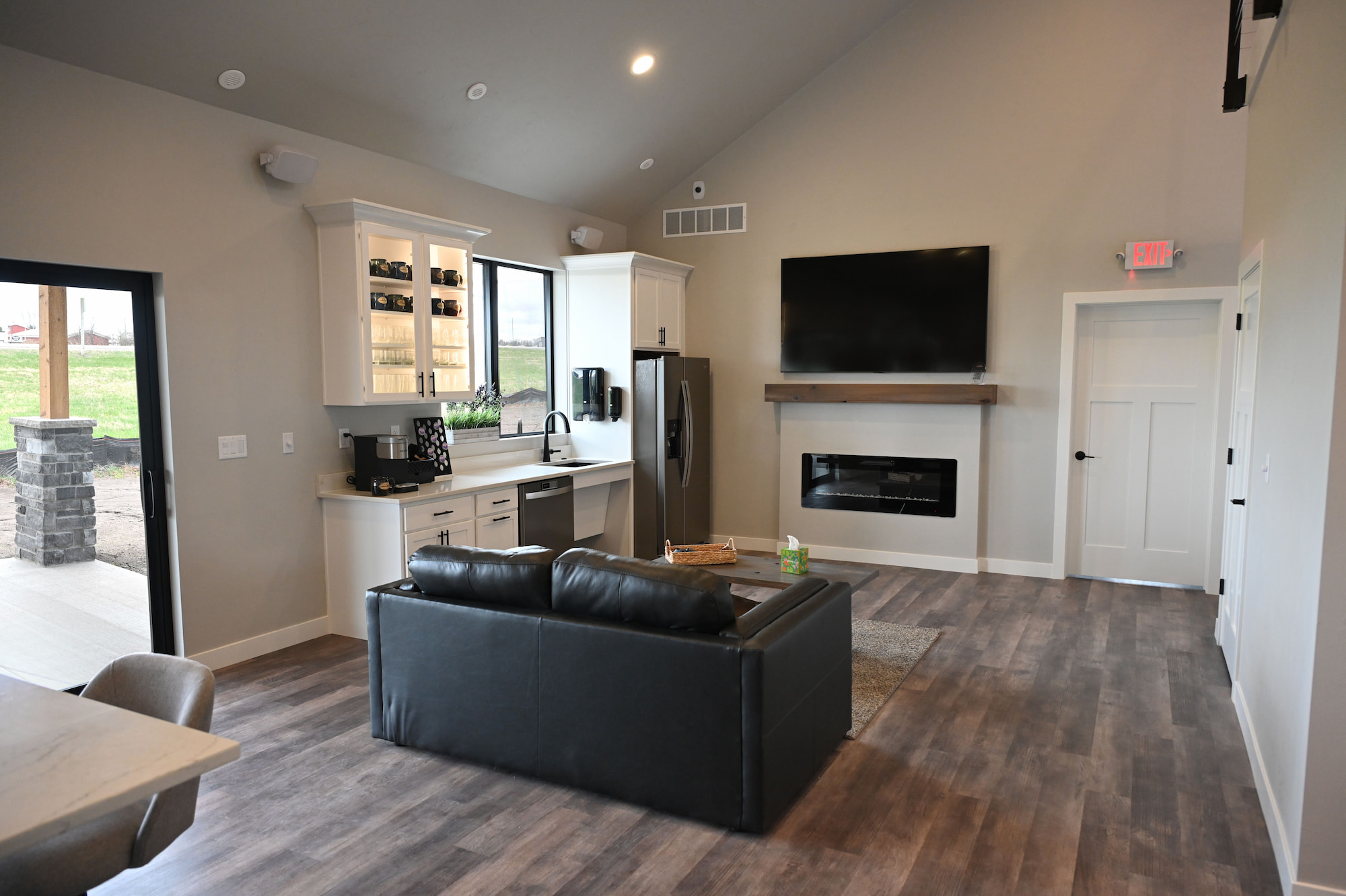 Open-concept commercial construction interior featuring a modern kitchen, meeting area with bar seating and leather couch