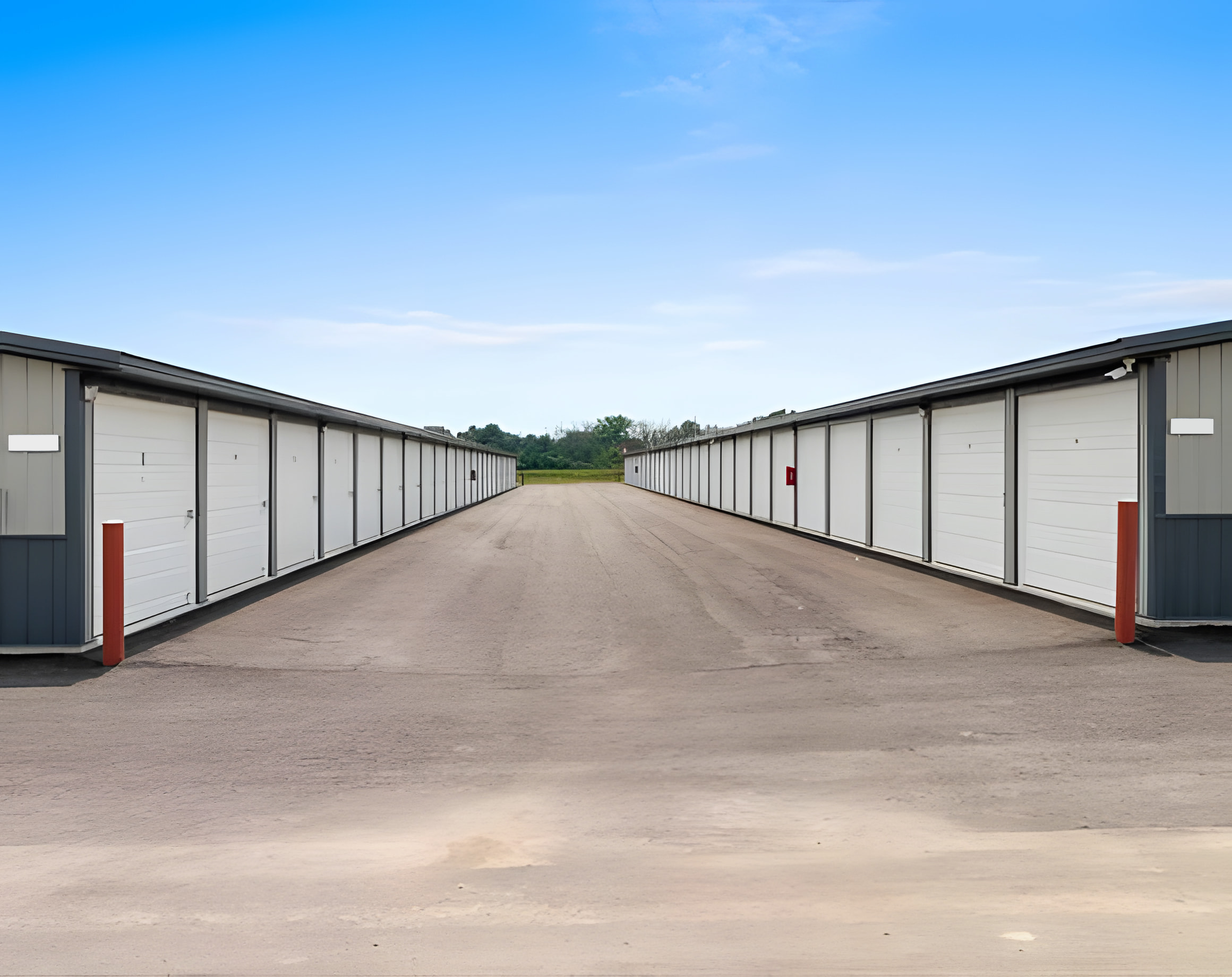 A long row of storage units with white doors and gray walls lines both sides of an asphalt driveway