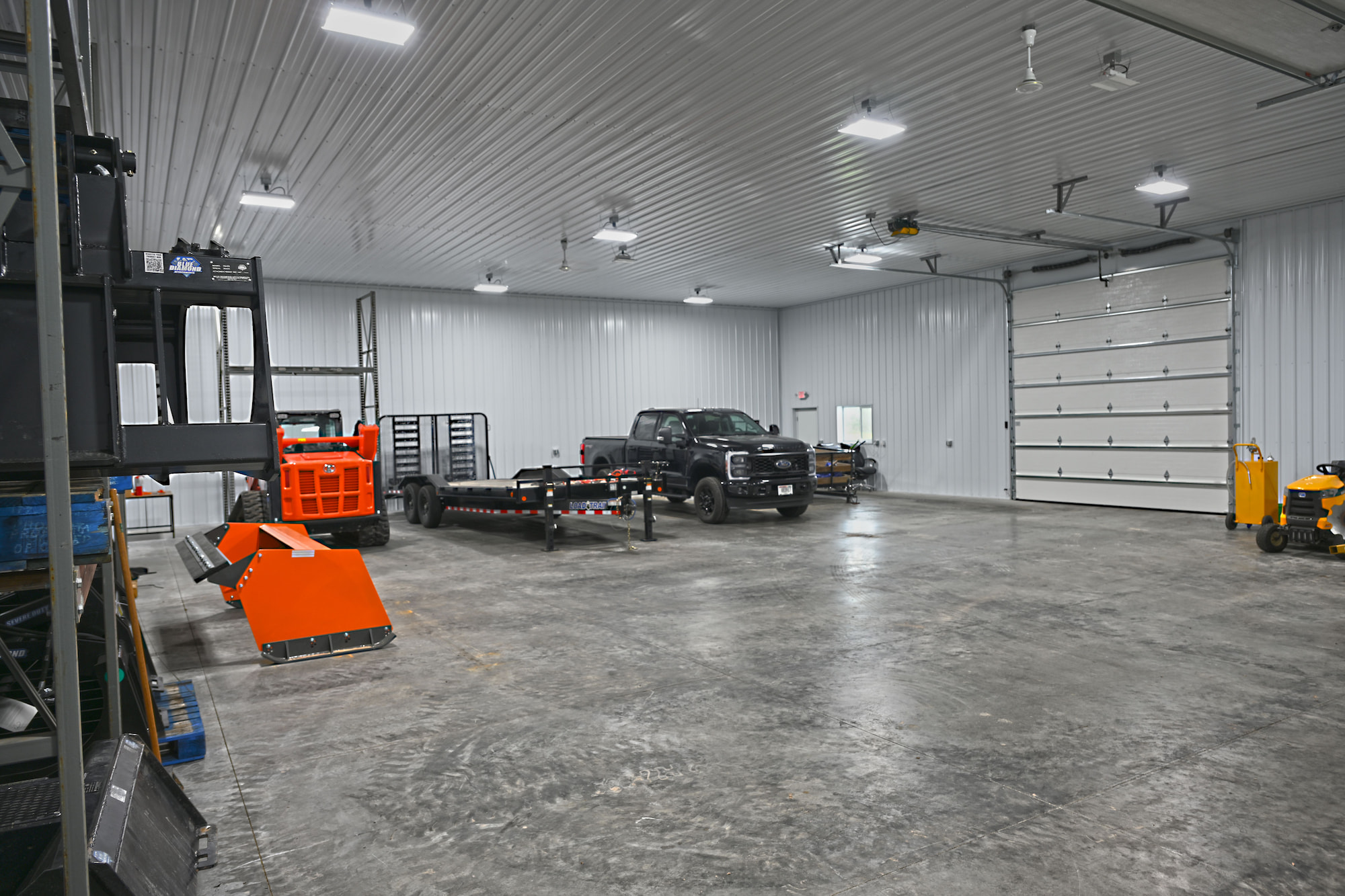 Wide shop bay in SkidSteers.com warehouse with Ford truck, trailer, skid steer, and overhead door.