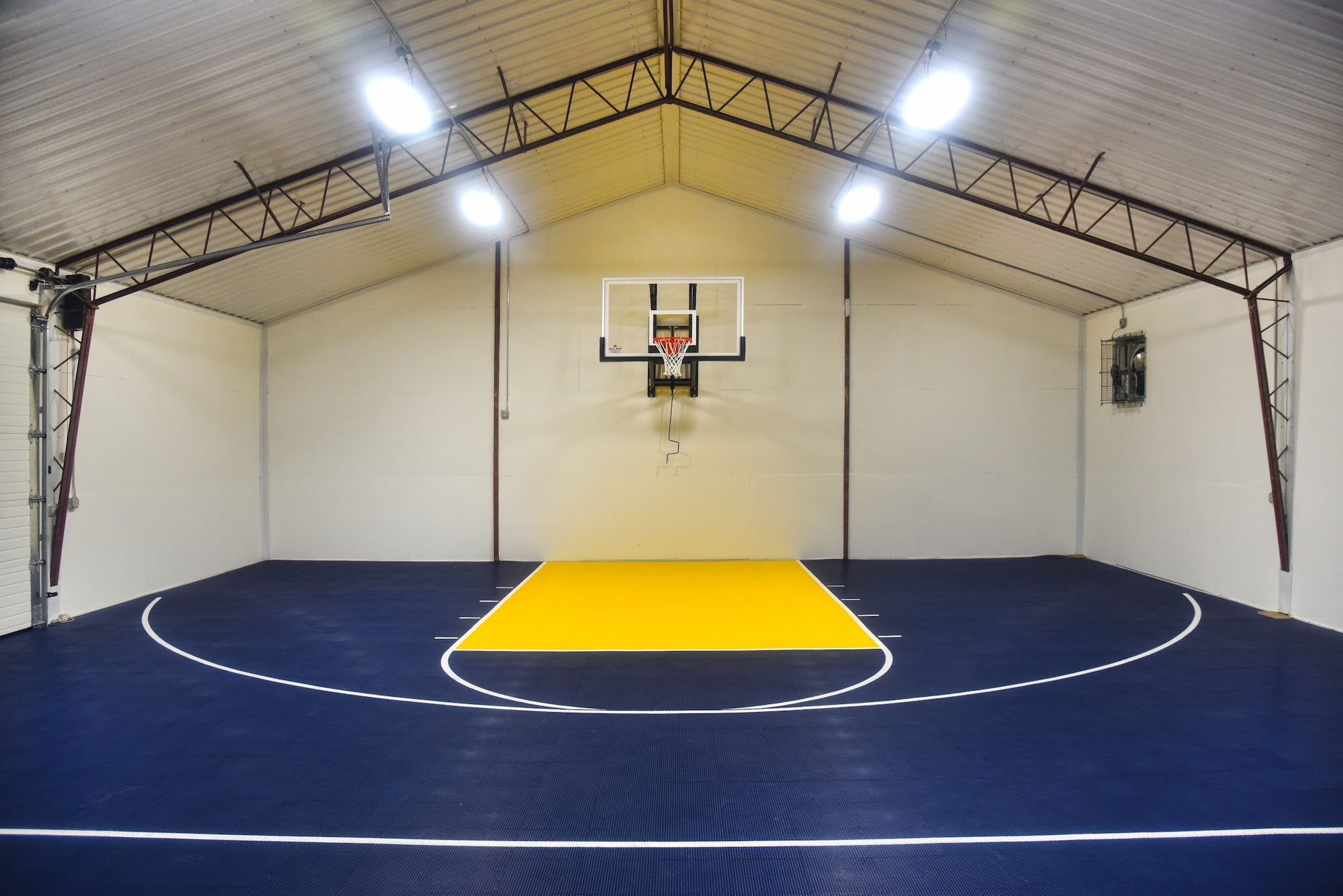 An old barn converted to sports practice facility with blue and yellow painted basketball court and basketball hoop mounted on wall.