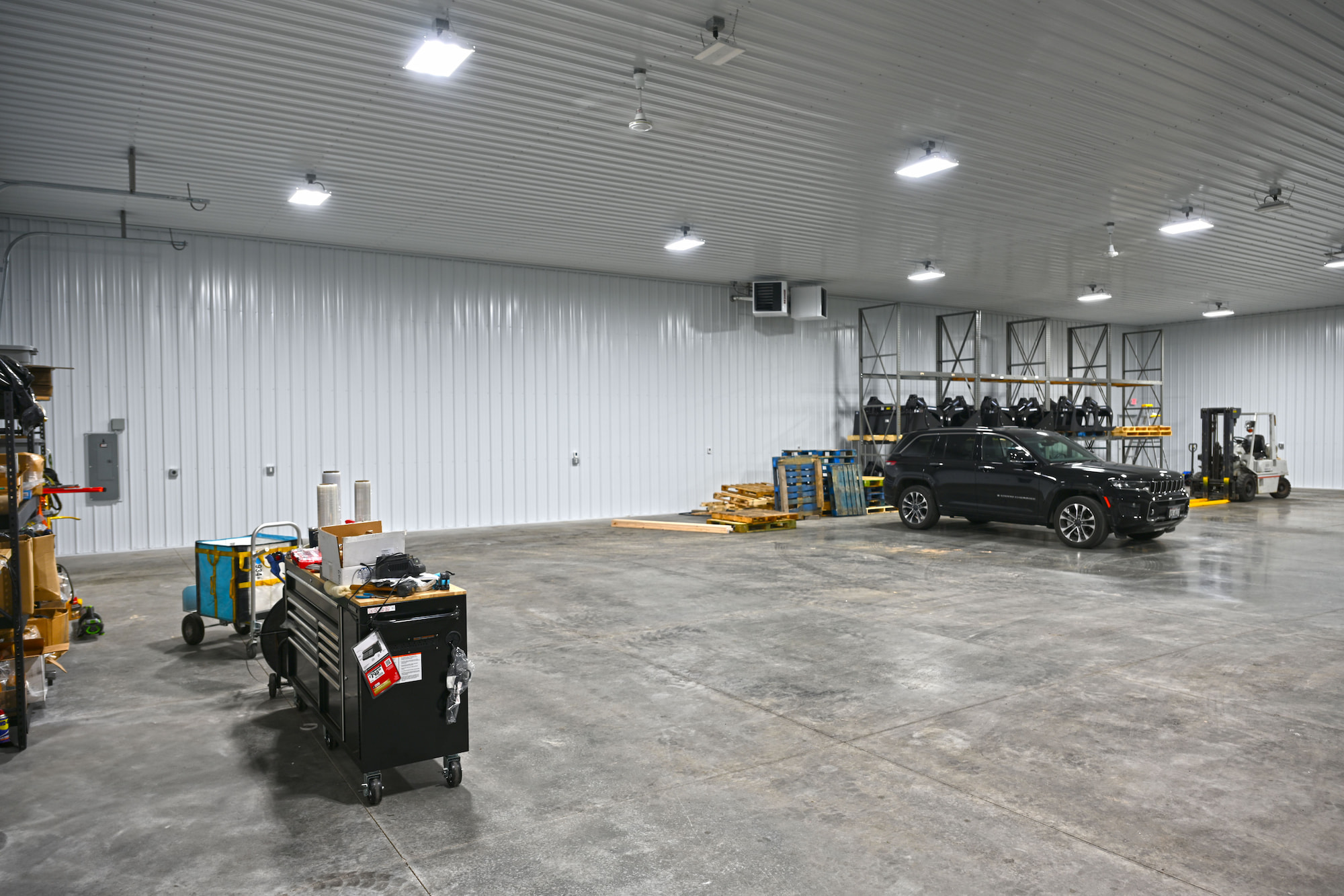 Spacious interior of SkidSteers.com warehouse with Jeep, forklift, pallet racks, and workbench tools.