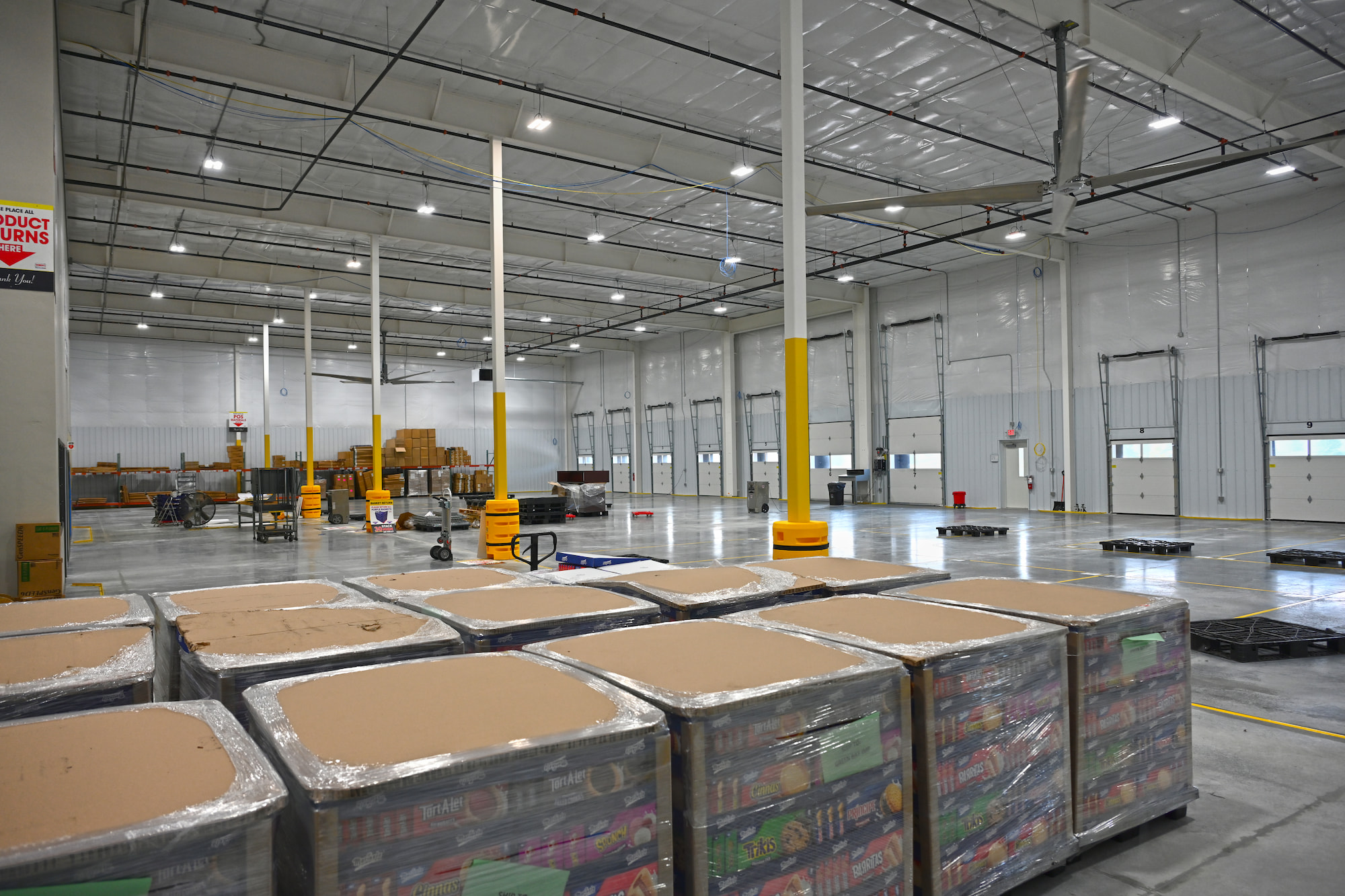 Interior of Kaukauna, WI warehouse with dock doors, palletized product storage, and overhead lighting.