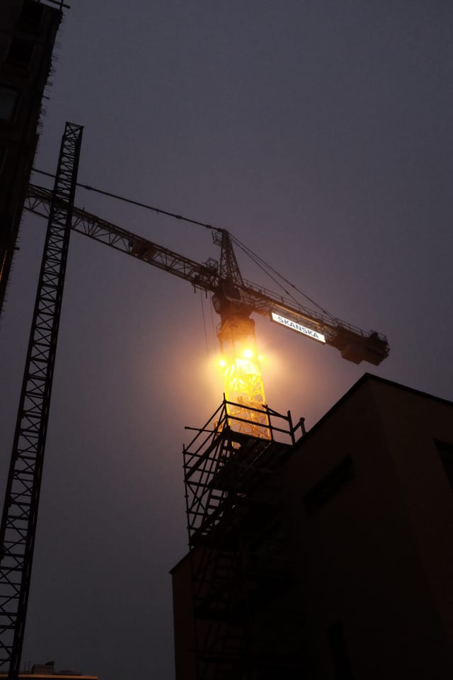 A crane standing in a dark sky, between shaded buildings.