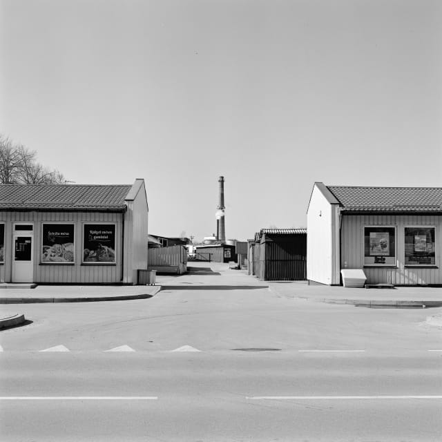 A view from the street onto some shops or market. Between the shops, in the distance, stands a chimney.