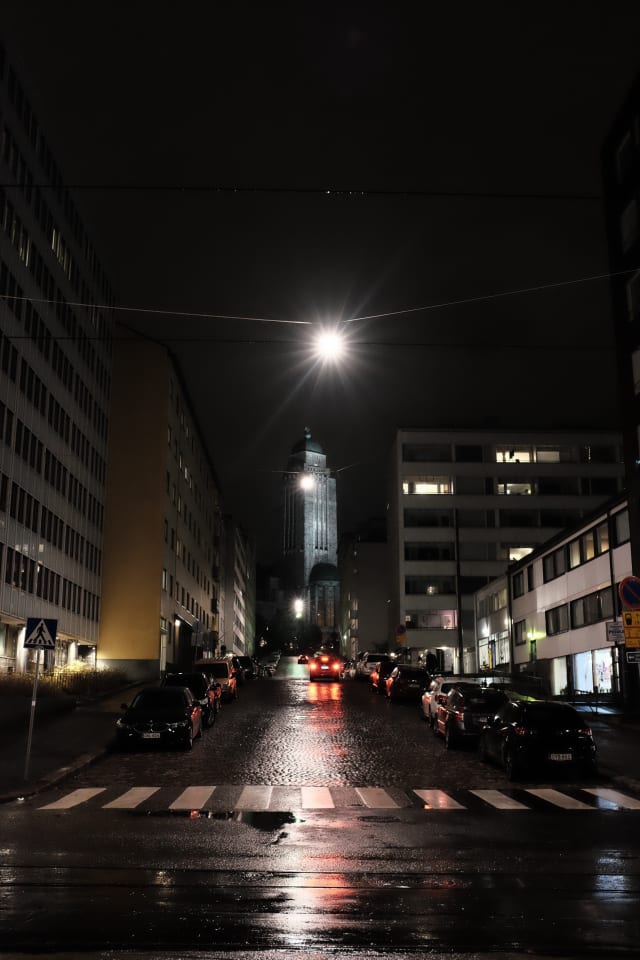 A pedestrian crossing, lit and reflective after rain. A church tower is in the distance.