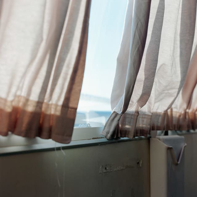 Two curtains on a ferry, a light pink or beige. They looks bit worn. Between them, a blue and white of the sea and sky beyond.