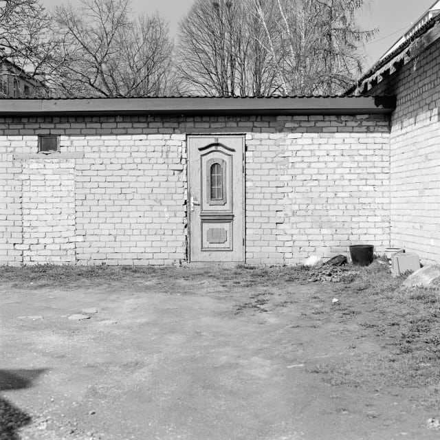 An ornate door, looking out of place in the middle of a brick wall. On its left, there is the outline of another, bricked-up door.