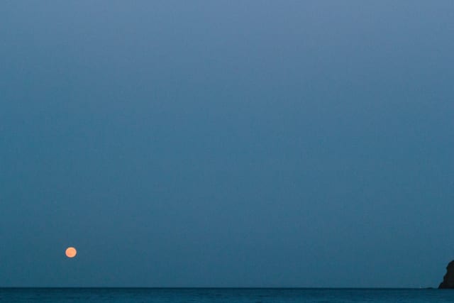 A bright, orange full moon on the left, over the sea.