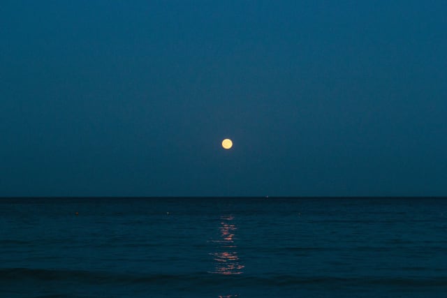 A full moon in the center, casting light over the shore.