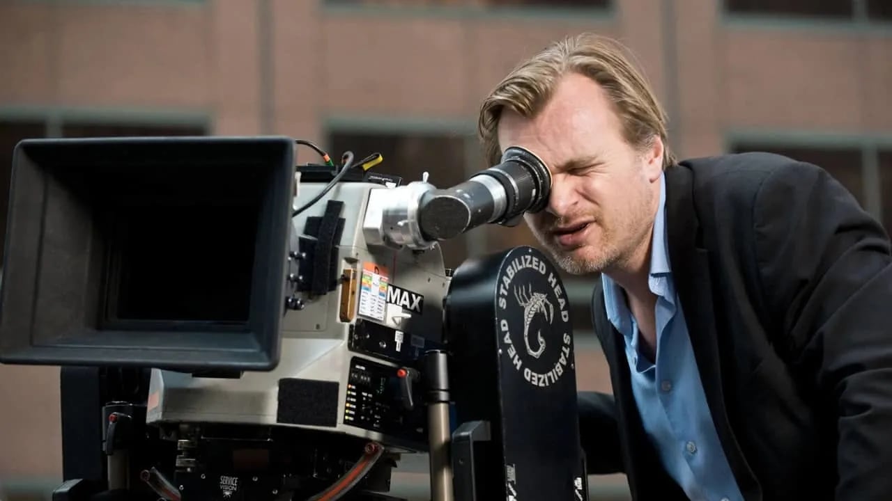 Christopher Nolan holding an IMAX camera in a projection booth, illustrating his IMAX obsession and the scale of the format.