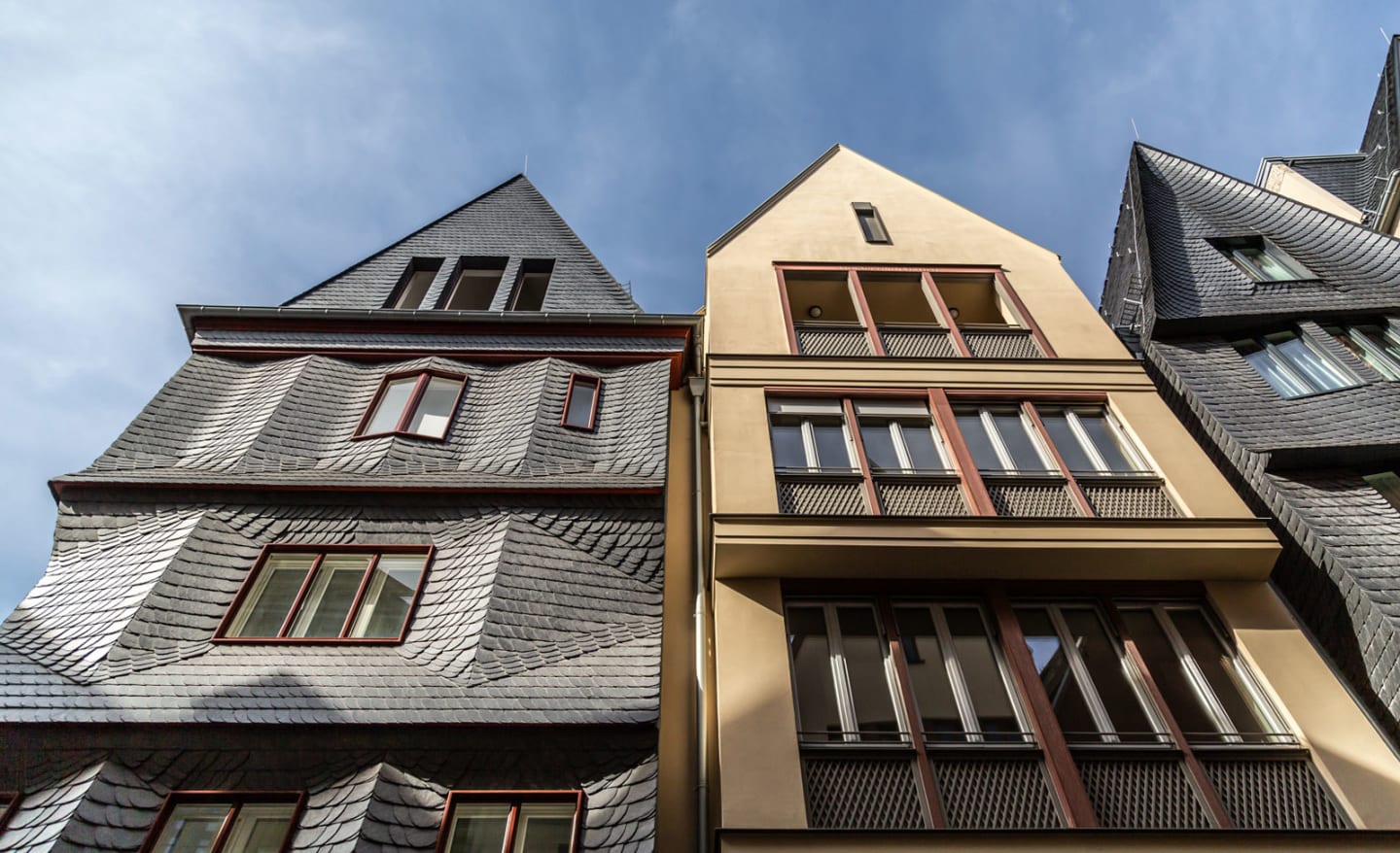 Facade view of modern buildings in Frankfurt’s new old town between the cathedral and the Römer, featuring slate roofs and clean geometric shapes under a blue sky