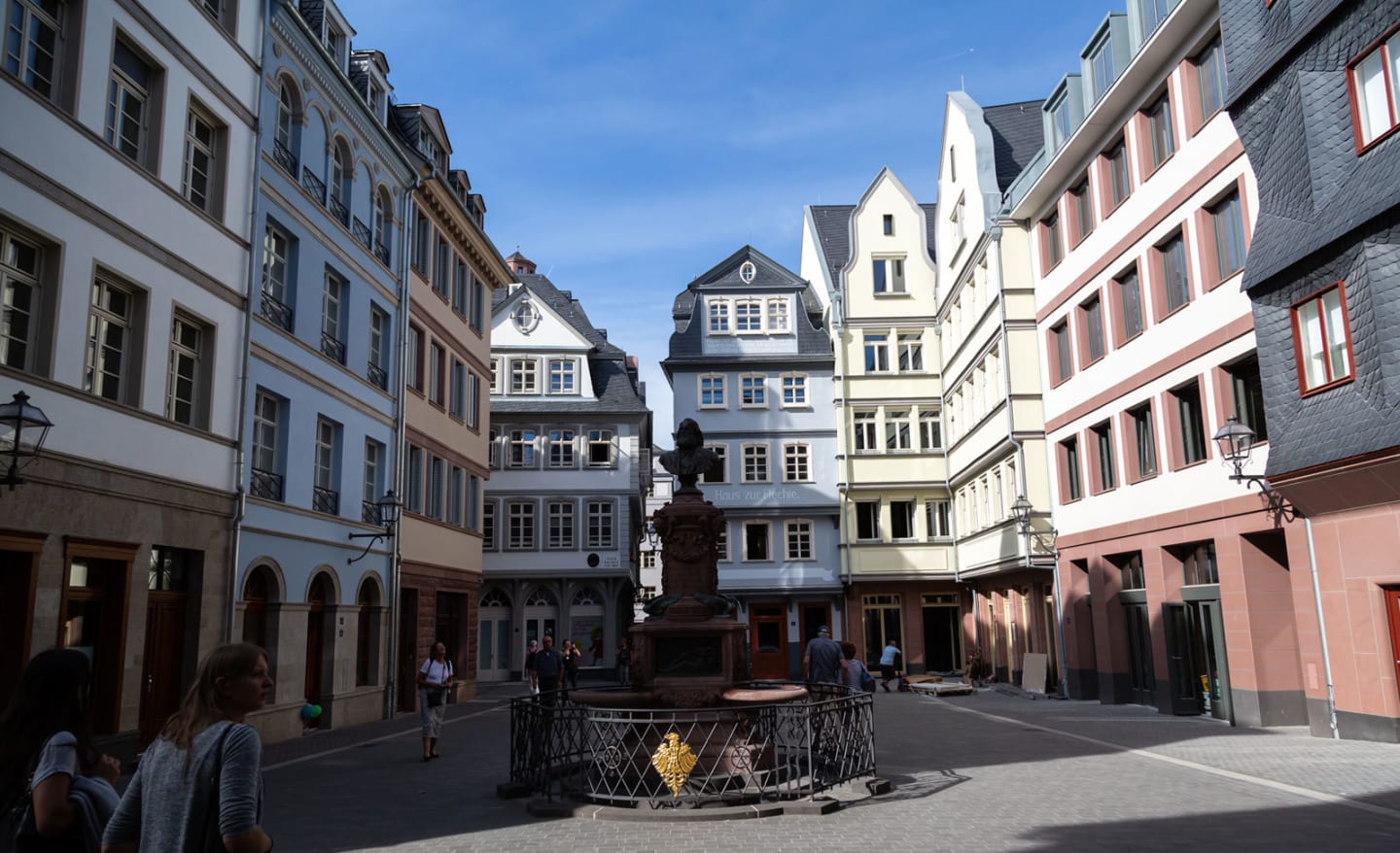 View of the so-called Hühnermarkt in Frankfurt’s old town featuring restored and newly built half-timbered houses, a central fountain, and pedestrians on a sunny day